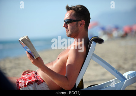 Un homme lit un livre tout en bronzant sur la plage de Patara Banque D'Images