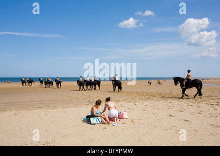 Une mère et sa fille pique-nique sur la plage à la station balnéaire anglaise comme une ligne de chevaux et leur montagne ride passé. Banque D'Images