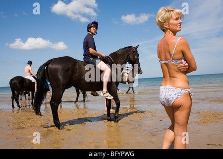 Une femme dans un bikini à motifs se tient près d'un jeune homme sur un cheval à côté de la mer. Banque D'Images