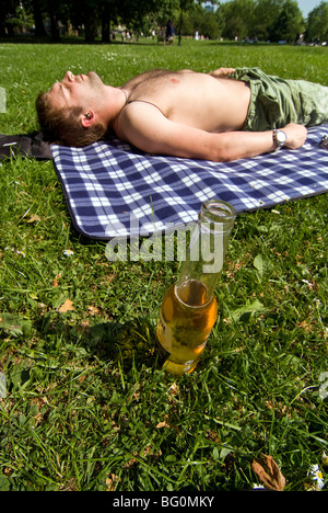 Young man relaxing in park avec une bouteille de bière Banque D'Images