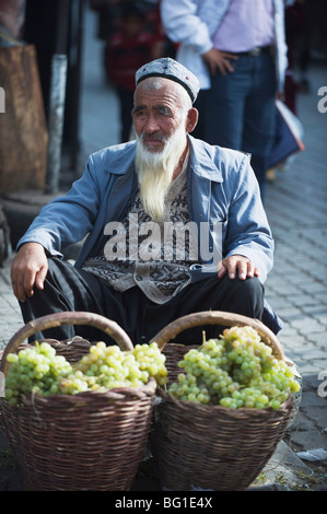 Homme barbu au raisin vente marché Dimanche, Kashgar (Kashi), la Province du Xinjiang, China, Asia Banque D'Images