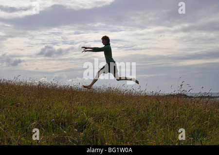 Jeune femme blanche sauter et sauter sur la dune les jambes dans l'air quelques corps dans l'espace au-dessus du sol Banque D'Images