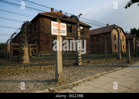 Clôture électrique périmètre & panneau d'avertissement à Auschwitz camp de la mort nazi. Oswiecim, Pologne. Hébergement pour les blocs sont derrière Banque D'Images