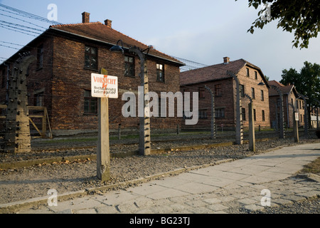 Clôture électrique périmètre & panneau d'avertissement à Auschwitz camp de la mort nazi. Oswiecim, Pologne. Hébergement pour les blocs sont derrière Banque D'Images