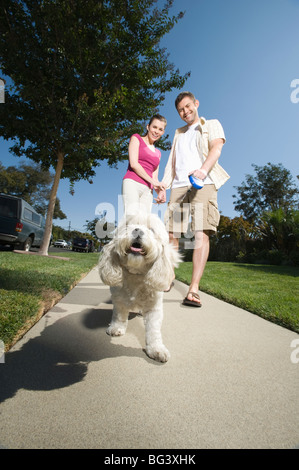 Couple walking dog le long trottoir Banque D'Images