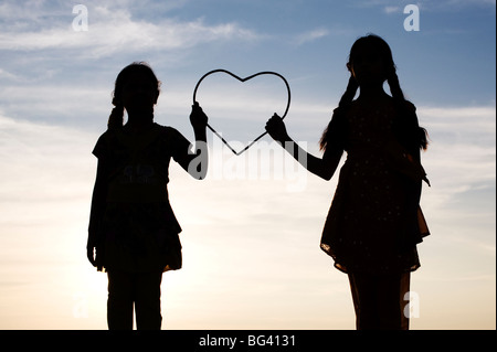 Silhouette d'un deux jeunes filles indiennes tenant un cœur au coucher du soleil. L'Inde Banque D'Images