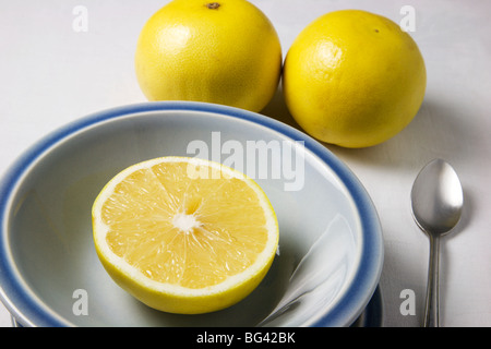 Un demi-pamplemousse dans un bol bleu et des pamplemousses entiers sur une nappe blanche Banque D'Images