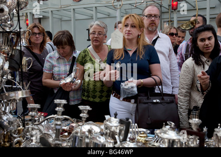 Les gens de consulter l'argenterie à un décrochage d'argent sur le marché de Portobello Road, Londres. Banque D'Images