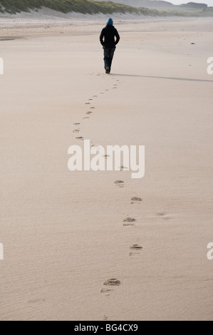 Une figure solitaire laisse des empreintes de pas sur la plage de sable en Northumbrie Bamburgh England UK Banque D'Images