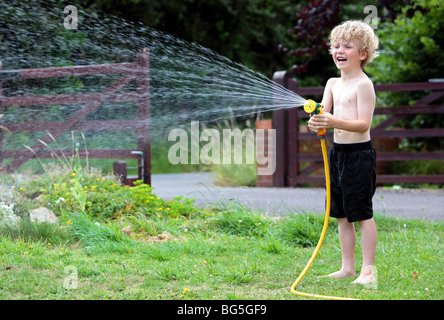 Young caucasian garçon blond jouant avec de l'eau dans un jardin et de rire Banque D'Images