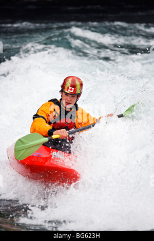 Andrew Jobe pagaies de kayak une par une vague sur la rivière Kananaskis, comté de Kananaskis, Alberta, Canada Banque D'Images