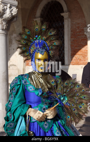 Close-up d'une femme vénitienne portant un masque d'or et d'un costume bleu et vert décoré de plumes de paon, Carnaval de Venise Banque D'Images