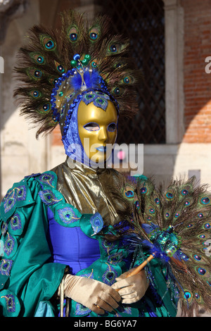 Close-up d'une femme vénitienne portant un masque d'or et d'un costume bleu et vert décoré de plumes de paon, Carnaval de Venise Banque D'Images