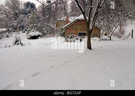 Paysage de neige scène, avec des empreintes profondes dans la neige vierge avec un chêne de style tudor grange, sciage empilées à côté en Angleterre Banque D'Images