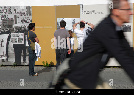 Allemagne, Berlin, Friedrich Strasse, Checkpoint Charlie, les touristes la lecture sur mur de Berlin, Berliner Mauer, Cyclist Banque D'Images