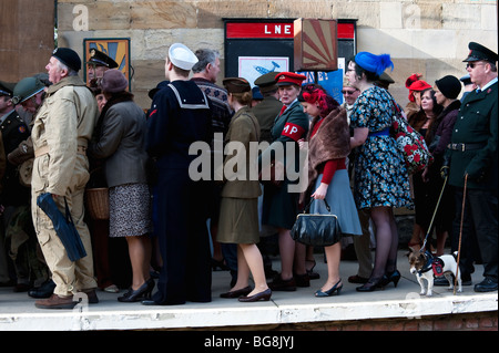 Un groupe d'interprètes historiques en costumes des années 40, la mise en queue sur un quai de gare à la fin de la guerre de Pickering dans Yorkshire du Nord. Banque D'Images