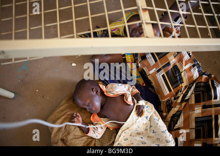 Un enfant souffrant du paludisme se trouve sur le sol de l'hôpital avec sa mère en Amuria, Ouganda, Afrique de l'Est Banque D'Images