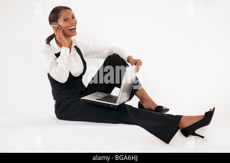 Jeune femme assise sur le sol à l'aide d'ordinateur portable et le port de casque bluetooth. Format horizontal. Banque D'Images