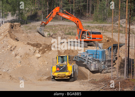 Production à la sablière ; la pelle charge les pierres et le sol vers le concasseur / séparateur de roches et le chargeur frontal collecte le gravier prêt , Finlande Banque D'Images