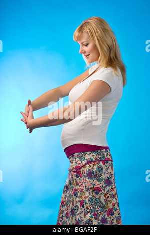 Shining happy pregnant woman standing latéralement sur fond bleu Banque D'Images