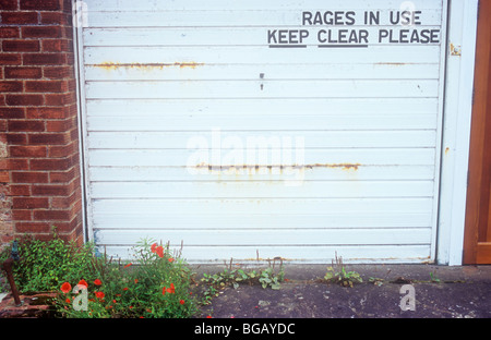 Porte de garage de rouille avec les mauvaises herbes et coquelicots de plus en face d'elle et signer la lecture fait rage dans la région de vente Restez clair veuillez Banque D'Images