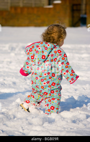 Baby Girl dans la neige vêtu d'un manteau chaud coloré Banque D'Images