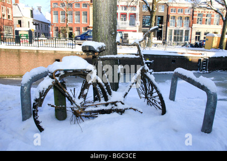 Rusty bike debout contre contre un arbre dans la neige Banque D'Images