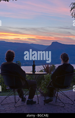 Couple assis à une table de patio en attente de verres donnant sur les vignes de Lang Vineyards et Okanagan Lake at sunset, Na Banque D'Images