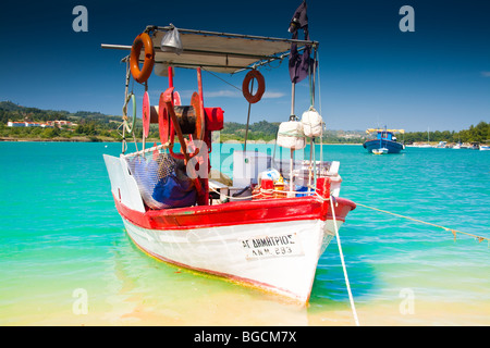 Un rouge et blanc peint en bateau de pêche est amarré sur une plage dans une lagune. Dans l'arrière-plan est un bateau bleu posés sur une mer d'azur. Banque D'Images