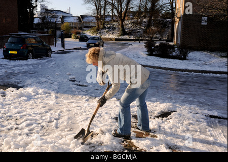 Femme enlevant la neige et la glace de son chemin et conduire à l'aide d'une pelle à Brighton UK clearing pelleter spade dig hiver froid Banque D'Images