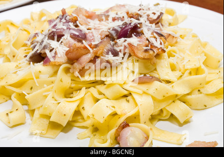 Assiette de tagliatelles sautées dans l'huile d'olive et au pesto avec lard grillé et oignon rouge. Garni de fromage parmesan râpé. Banque D'Images