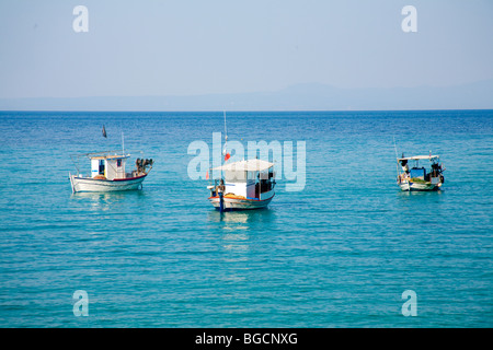 Trois bateaux de pêche lumineux se trouvent amarrés dans une baie de couleur bleu azur, dansant sur le léger gonflement paresseusement. Banque D'Images