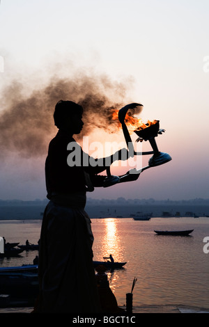 Prêtre hindou adorant Dieu soleil Surya au lever du soleil sur la rive de la rivière Ganges (Mère Ganga) à Varanasi, Inde. Banque D'Images