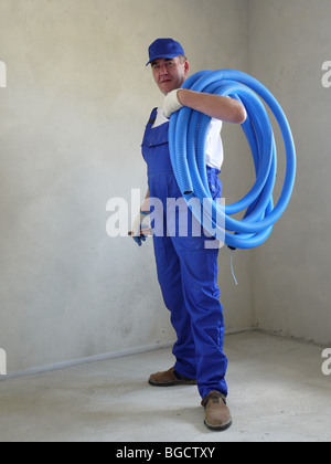 Electricien portant une chemise blanche, bouchon bleu uniforme bleu et posant avec bobine de câble PVC ondulé flexible tuyau de protection Banque D'Images