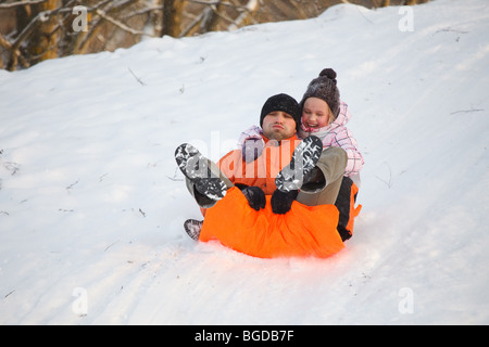 Père et fille s'amusant en hiver en faisant glisser en bas de la colline Banque D'Images