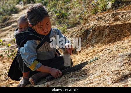 Petite enfant avec un bébé sur son dos, assis sur un sentier dans les montagnes du nord du Vietnam près de la ville de montagne de sa Pa, Viet Banque D'Images