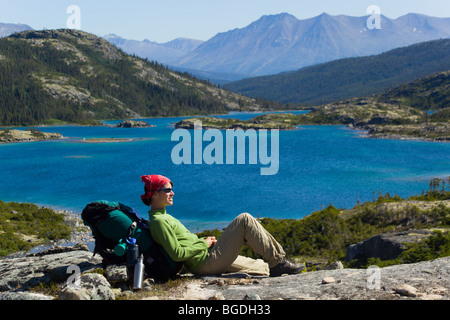 Jeune femme, randonneur, backpacker reposant, appréciant panorama sur lac profond, historique du col Chilkoot, piste, Territoire du Yukon Banque D'Images