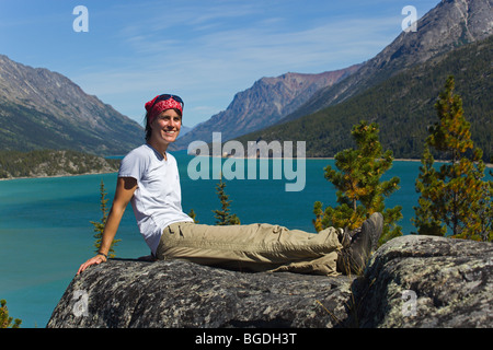 Jeune femme, randonneur, backpacker sitting on rock, se reposer, profiter de panorama sur le lac Bennett, le col Chilkoot, lieu historique Banque D'Images