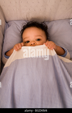 3 1/2 mois garçon couché dans son lit et de se cacher sous sa couette. Banque D'Images