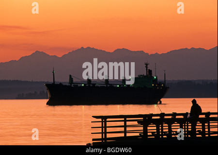 La silhouette du pier avec man fishing off pier au coucher du soleil sur le Puget Sound avec montagnes olympiques de l'État de Washington Seattle USA Banque D'Images