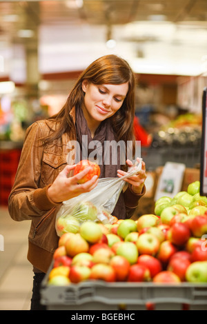 Une femme dans une épicerie est l'examen d'une apple avant l'achat. Banque D'Images
