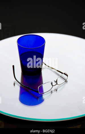 Verre de l'eau bleu et les lunettes sur la Table ronde de réflexion brillant Banque D'Images