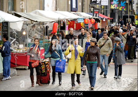 Les visiteurs passant des aliments ethniques de vendeurs de rue au quartier de l'ancienne brasserie Trueman. Londres. La Grande-Bretagne. UK Banque D'Images