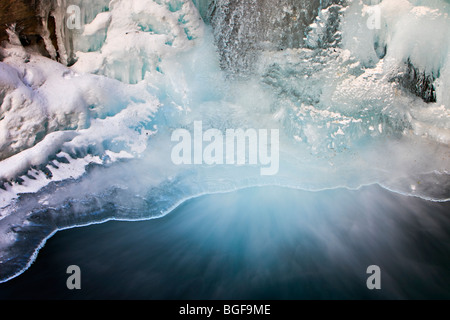 Lower Falls partiellement gelé de la Johnston Creek pendant l'hiver avec de l'eau qui s'écoule dans un bassin à la base, entourée de glace f Banque D'Images