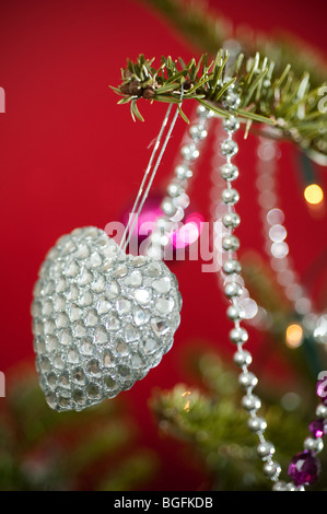 Une en forme de coeur couleur décorations babiole joliment placé sur un pin (arbre de Noël sur fond rouge. Banque D'Images