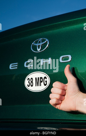 Close up of person holding Thumbs up près de 38 miles par gallon de carburant autocollant sur Toyota Echo vert voiture. Banque D'Images