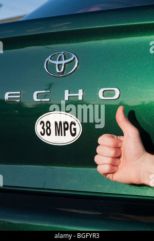 Close up of person holding Thumbs up près de 38 miles par gallon de carburant autocollant sur Toyota Echo vert voiture. Banque D'Images