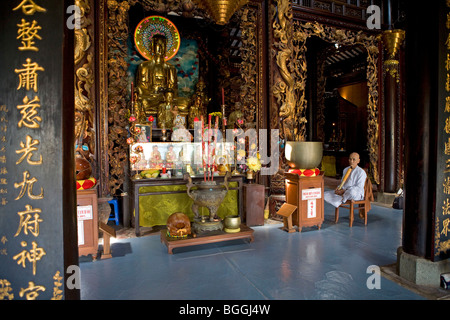 Mann, assis près d'un autel dans un temple bouddhiste, Vietnam Banque D'Images