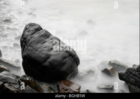 Belles images d'art créé par une longue exposition de vagues déménagement autour d'un énorme rocher et rochers sur une plage au crépuscule écossais Banque D'Images