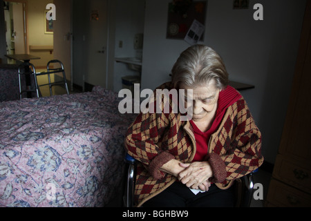 Femme âgée est assis dans sa chambre à une maison de soins infirmiers, perdu dans ses pensées. Banque D'Images